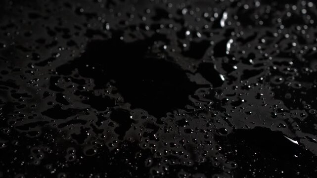 Dark water droplets create unique patterns on a reflective surface during a quiet moment at night