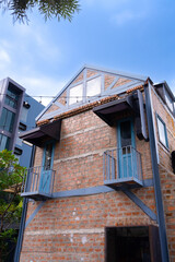 Rustic brick house with blue doors and balconies under clear sky, surrounded by greenery and modern buildings, creating peaceful urban scene