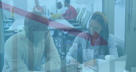Reviewing docs, two coworkers, woman wearing headband button-up at boardroom with laptop and charts