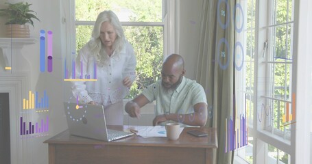 Leaning woman in white blouse, man reviewing laptop charts at home study with papers and mug