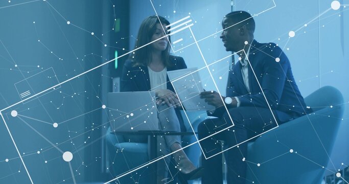 Sitting pair wearing blazers reviewing document in office lounge with laptop and digital overlay