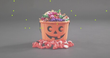 Fototapeta premium Displaying orange pumpkin bucket spilling foil candies and red-and-white sweets on gray tabletop