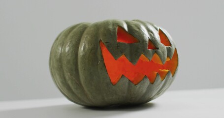 Glowing carved green-gray pumpkin sitting on smooth white tabletop, showing orange internal glow © vectorfusionart