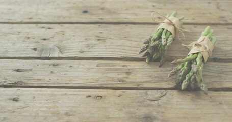 Lying two asparagus bundles wrapping kraft wraps, tying twine on worn plank with knots, copy space