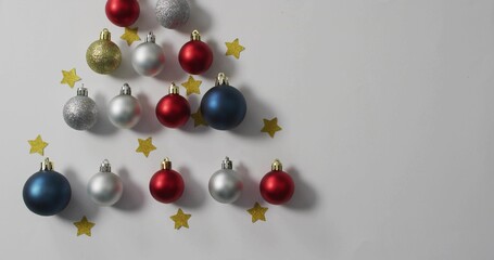 Fototapeta premium Displaying triangular red silver blue gold baubles with metal caps on white tabletop, copy space