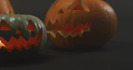Fototapeta premium Glowing pair of carved jack-o'-lantern pumpkins casting warm light, showing internal glow in studio