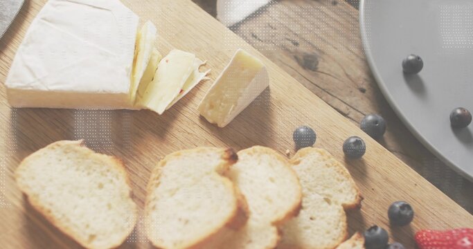 Displaying brie wedge resting on wood cutting board, with toasted crostini and loose blueberries
