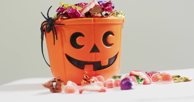 Sitting orange pumpkin bucket holding wrapped candies and gummy teeth on tabletop, with spider