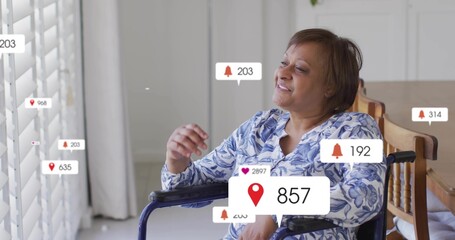 Smiling woman in wheelchair leaning toward shutters at home, in blue top, viewing alerts by table
