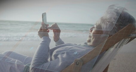 Fototapeta premium Reclining senior woman using smartphone on deckchair at shore in gray top, blue-overlay, copy space