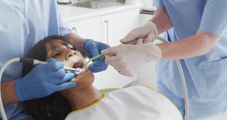 Treating dental team working over patient in clinic using drill and suction, bib, blue scrubs © vectorfusionart