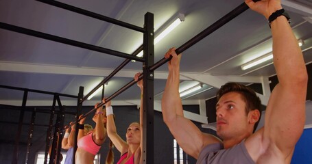 Performing pull-ups man on right gripping bar in gym rig, wearing workout clothes, copy space