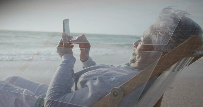 Reclining senior woman using smartphone on deckchair at shore in gray top, blue-overlay, copy space
