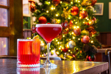 two Christmas themed cocktail drinks on a table with a blurred Christmas tree in the background