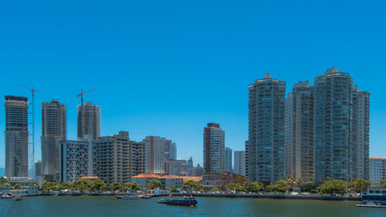 City skyline with modern skyscrapers and construction cranes reflecting urban development over the blue waterfront on a sunny day