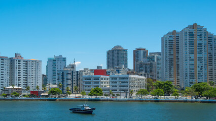 Fototapeta premium Coastal city with a dense skyline of modern high-rise buildings and skyscrapers overlooking the water, with a small boat in the foreground
