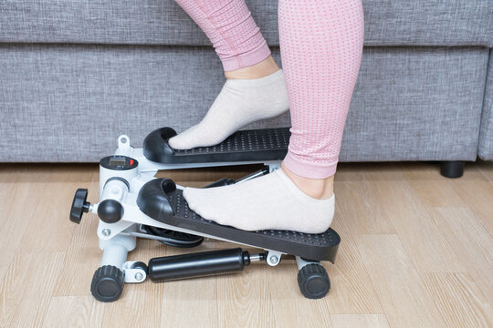 A woman in pink leggings and white socks walks on stepper at home, side view.