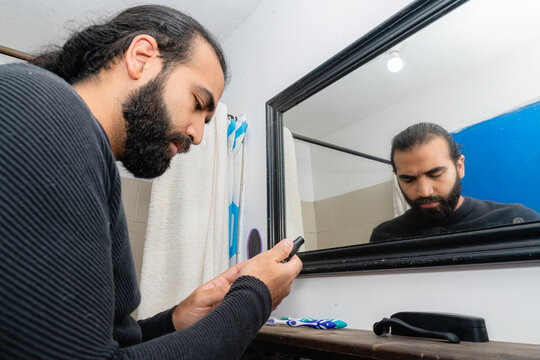 Colombian man with beard examining hair loss product containing minoxidil and finasteride in bathroom