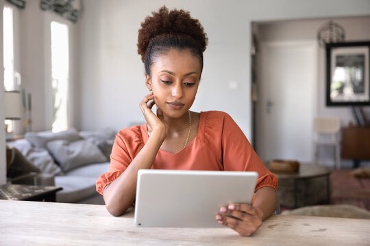 Pensive beautiful young African woman using digital tablet at home