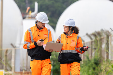 Safety inspectors reviewing operational data with laptop and radio at industrial site, Engineering staff conducting on-site inspection with protective gear and devices
