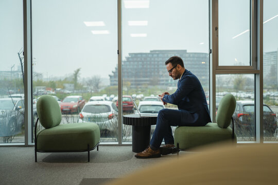 Businessman checking time on watch while waiting in corporate lounge - Powered by Adobe