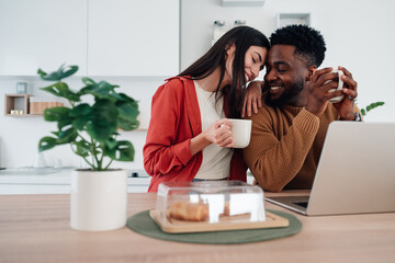 Loving interracial couple enjoying coffee and laptop at home