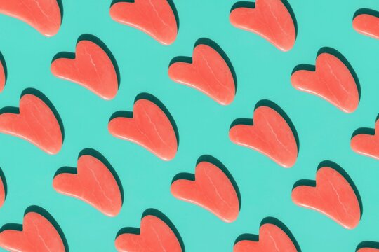 Colorful gua sha body tools arranged in a repeating pattern on a turquoise background. The tools are heart-shaped and made of a smooth material.