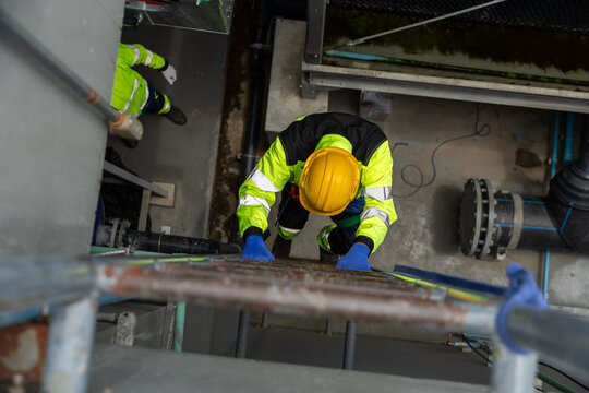 Industrial worker in safety gear climbing ladder inside factory. Concept of occupational safety, maintenance and engineering. Top view of technician in high visibility clothing. - Powered by Adobe