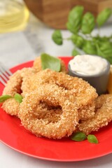 Deep fried squid rings with basil and sauce on light table, closeup