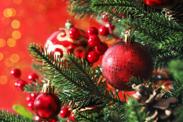 Beautiful ornaments on Christmas tree against red background with blurred lights, closeup. Bokeh effect