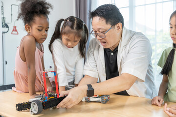 Teacher demonstrating robotics project to diverse group of children in STEM class. Concept of science education, technology learning, innovation and teamwork in early childhood development.