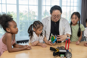 Teacher demonstrating robotics project to diverse group of children in STEM class. Concept of science education, technology learning, innovation and teamwork in early childhood development.