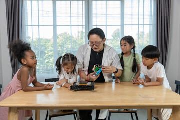 Teacher demonstrating robotics project to diverse group of children in STEM class. Concept of science education, technology learning, innovation and teamwork in early childhood development.
