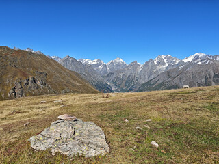 Rugged Alpine background panorama with a large weathered rock in the foreground, overlooking the dramatic, jagged snow-capped peaks of the Caucasus Mountains near Mestia, Georgia