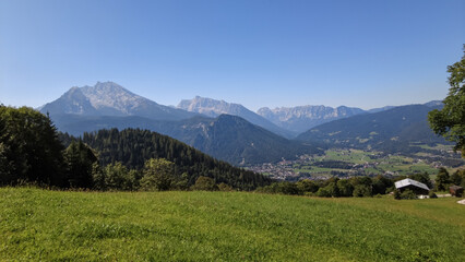 Breathtaking panoramic view of a lush green Alpine meadow overlooking a picturesque valley town and majestic mountain peaks under a vibrant blue sky in Austria
