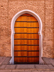 Traditional wooden door with detailed metal studs and an iconic Moorish arch set into a terracotta brick wall of a mosque in Marrakech, Morocco