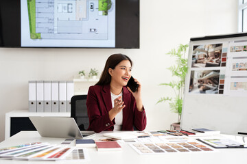 Happy interior designer speaking over the phone in her home office. Creative business woman taking notes during a phone call with her clients. Female designer working on a new project remotely.