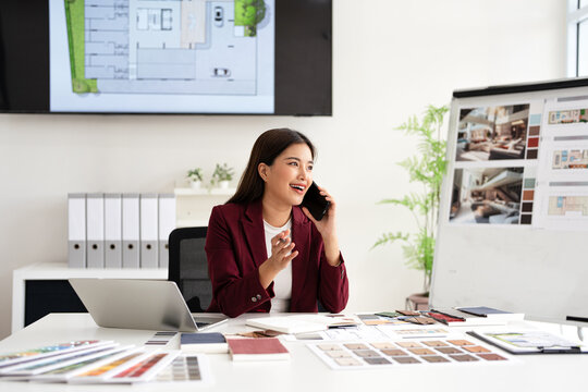 Happy interior designer speaking over the phone in her home office. Creative business woman taking notes during a phone call with her clients. Female designer working on a new project remotely.
