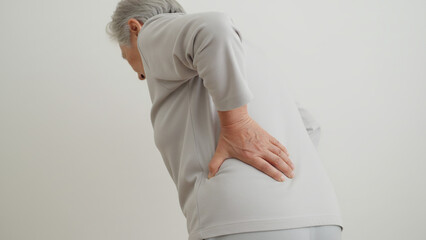 Senior adult bending slightly forward with one hand supporting the lower back