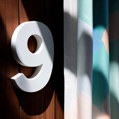 A large white number nine is mounted on a wooden surface, with sunlight casting shadows. Colorful curtains are visible in the background.