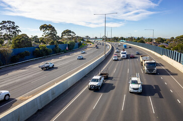 Princes Freeway at Laverton North in Melbourne, Australia, showing multi-lane traffic. Wide divided highway with sound barriers, concrete median. Concept of commuting, road infrastructure