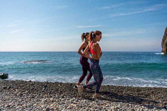 Running fitness women jog together on a rocky pebble beach for summer outdoor workout - Powered by Adobe