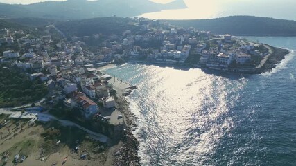 Aerial drone view of a traditional coastal village on Thassos island in Greece. Sunlight reflecting on the sea, dense hillside houses and clear Mediterranean shoreline - Powered by Adobe