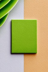 Abstract composition featuring a green square on a textured leather surface with a green leaf in the corner. The background is divided into white and orange sec
