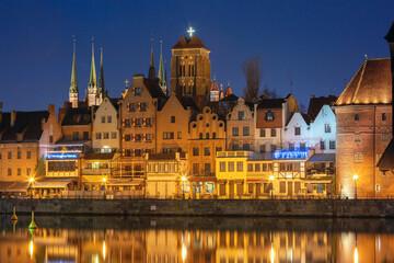 Fototapeta premium Historic waterfront houses and illuminated church towers in the old town of Gdansk Poland at night