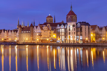 Fototapeta premium Historic waterfront houses and illuminated church towers in the old town of Gdansk Poland at night