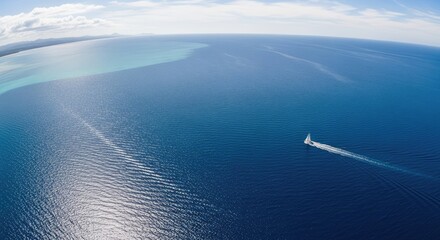A sailboat sailing on a vast, blue ocean with a clear sky in the background.