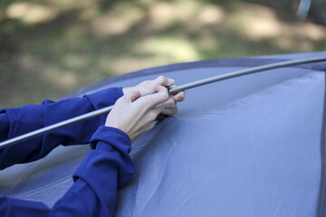 Focused woman hand setting up blue tent pole for camping in forest. An outdoor activity and adventure for summer vacation, preparing campsite for night