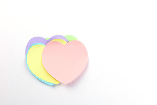 Top view, flat lay with copy space of a charming stack of pastel heart-shaped sticky notes on a clean white background, offering ample copy space for love notes, reminders, or heartfelt messages.
