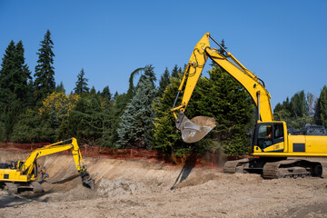 Two large excavators working on digging out a large foundation pit for a stormwater retention system, earthworks construction project site on a sunny day

